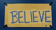 Team logo is a tan poster pinned to a blue wall. The word BELIEVE is hand written in capital letters on the tan poster. Team logo is a tan poster pinned to a blue wall. The word BELIEVE is hand written in capital letters on the tan poster.